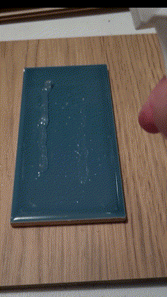 Spraying glass cleaner on a mechanically removed bead of silicone to test if any residue remains.